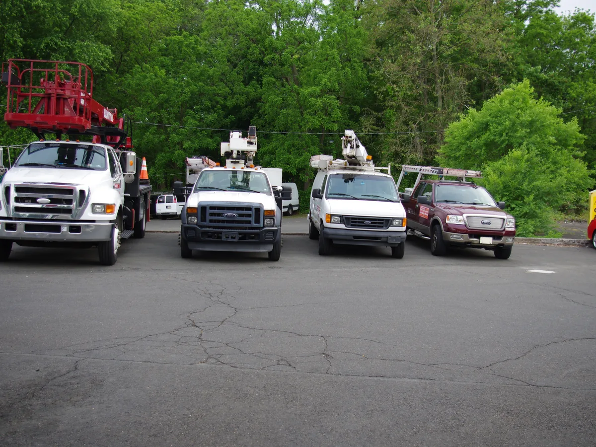 The VH Sign and Lighting truck fleet lined up in the yard, including the crane truck and two bucket trucks