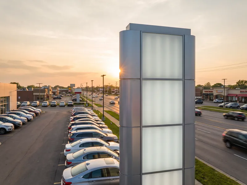 An illuminated dealership pylon sign rising above rows of inventory at an auto dealership