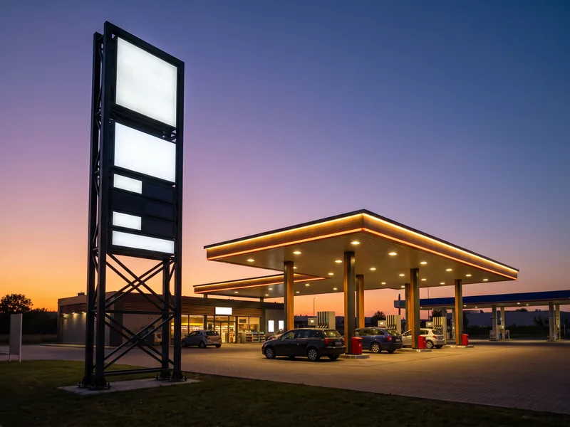 A gas station pricing pylon at dusk beside a lit fuel canopy