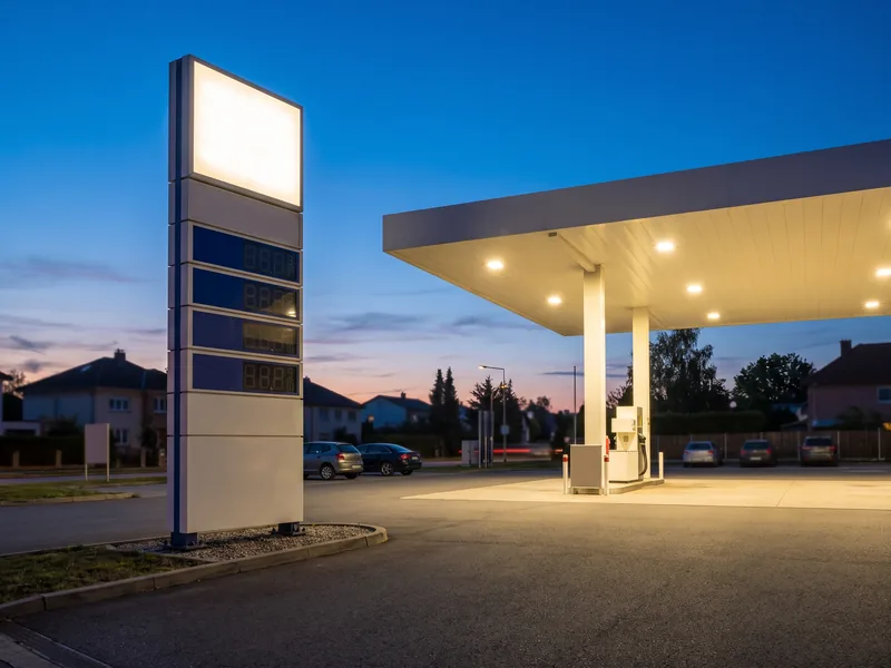 A gas station pricing pylon beside a lit fuel canopy at dusk