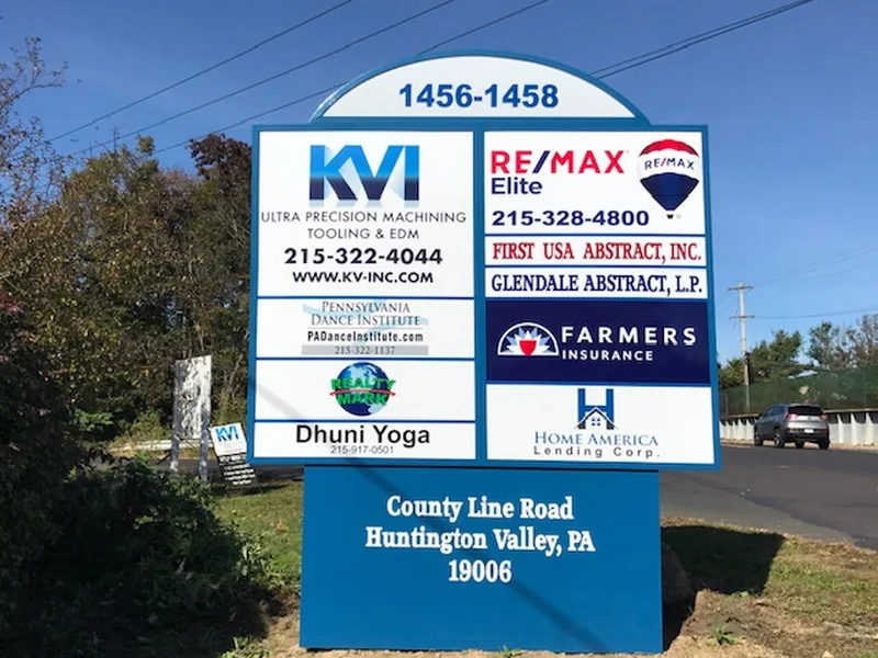 Multi-tenant pylon sign with an arched blue cap reading 1456-1458 above nine tenant panels including KVI and RE/MAX Elite, on a blue base lettered County Line Road, Huntington Valley, PA 19006