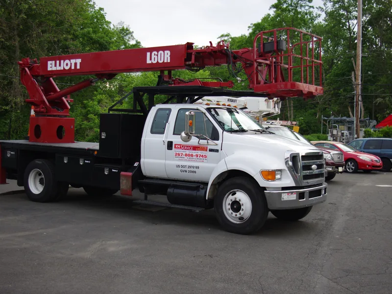 VH bucket truck with its boom raised, positioned for a storefront sign installation