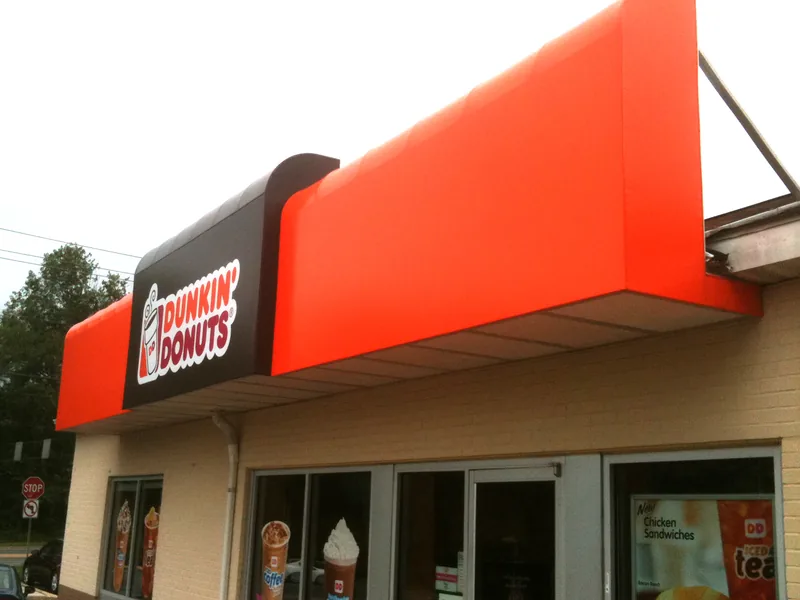 Orange illuminated Dunkin Donuts awning wrapping the corner of a storefront
