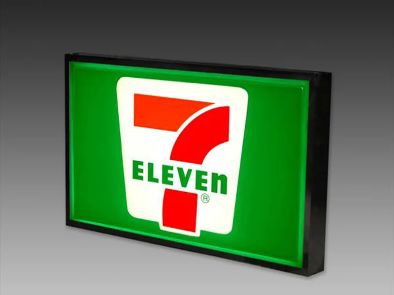 Illuminated 7-Eleven light box cabinet sign glowing against a dark wall